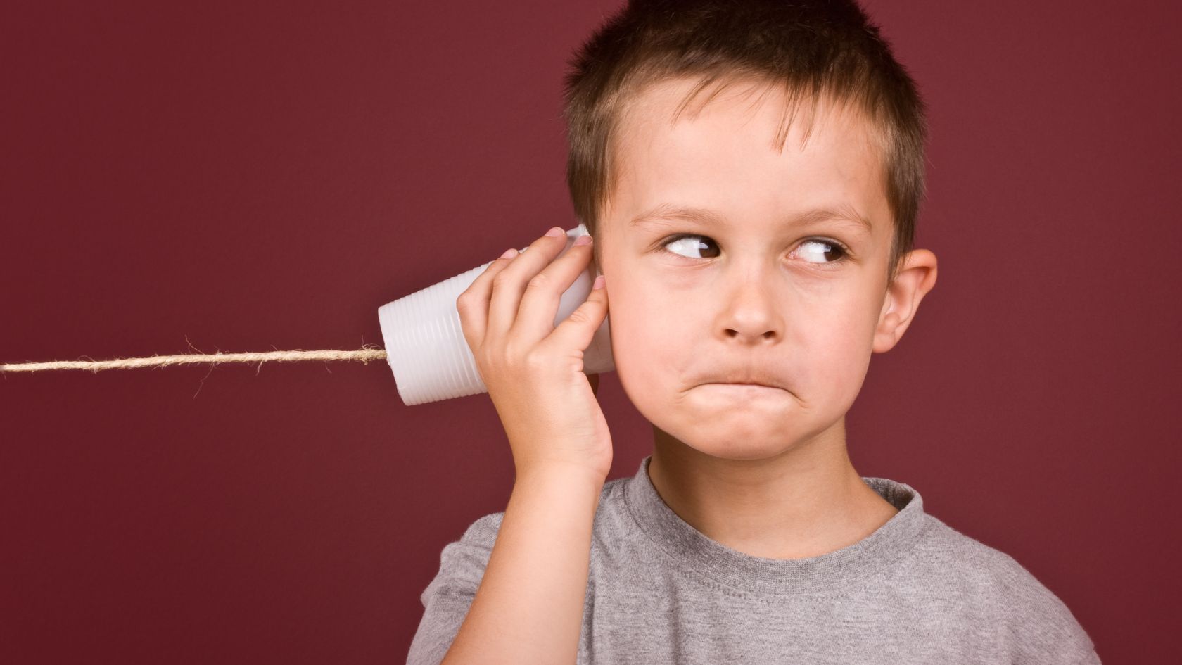 A young boy holds a plastic cup to his ear, connected via string to create a basic communications device